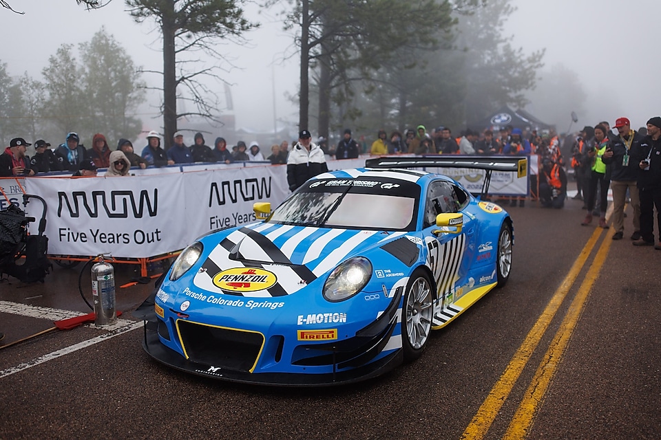 A blue race car on a road with people watching