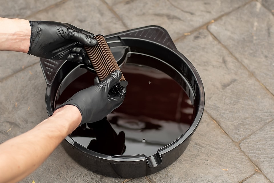 Man holds a filter and oil bucket is on the floor