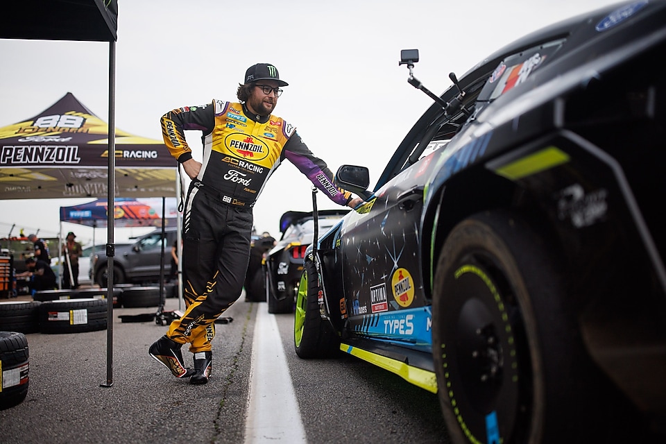 Man in racing suit leaning against racecar