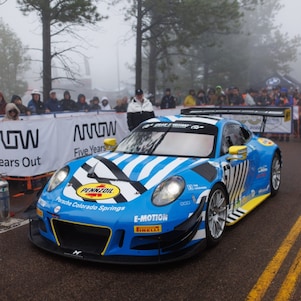 A blue race car on a road with people watching